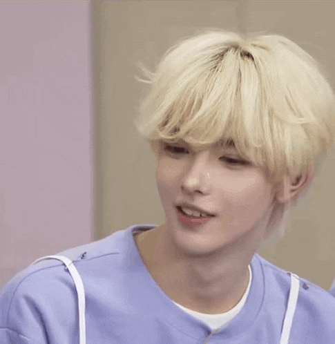 a young man with blonde hair is smiling and wearing a blue shirt