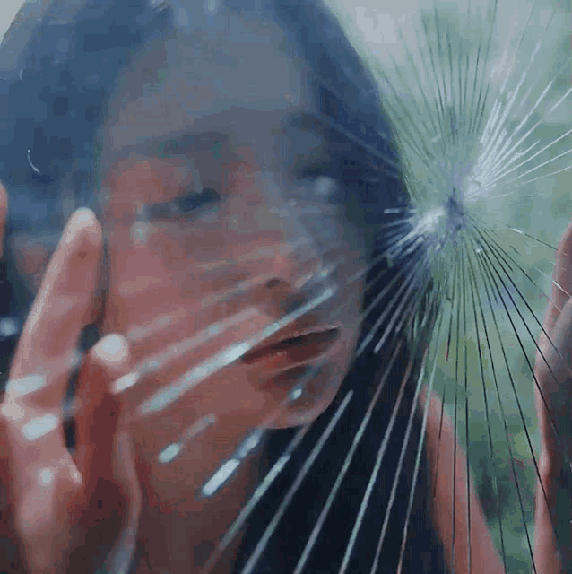 a woman is looking through a broken glass window