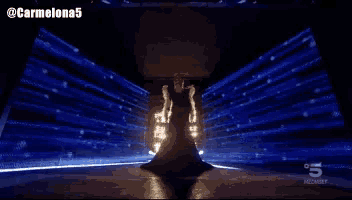 a woman in a long dress is standing in front of a screen that says ' 5 ' on it