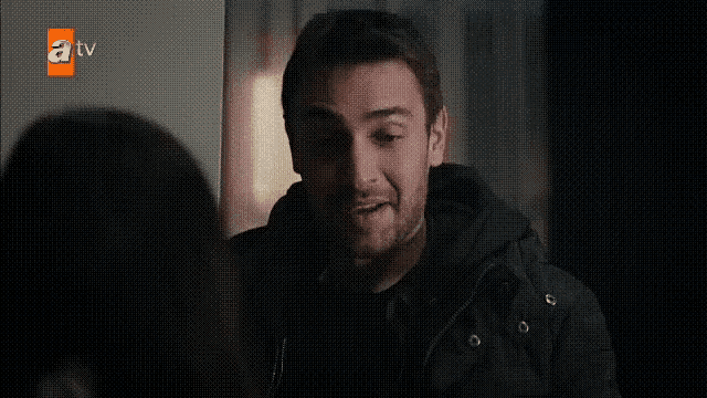 a man in a black jacket talking to another man in a dark room .