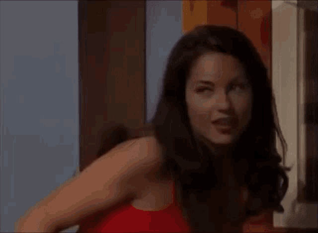 a woman in a red tank top is standing in a room and making a funny face .