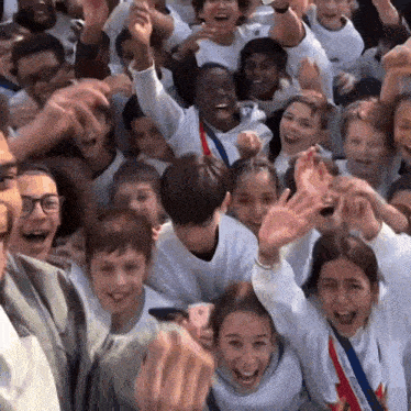 a large group of children are raising their arms in the air .
