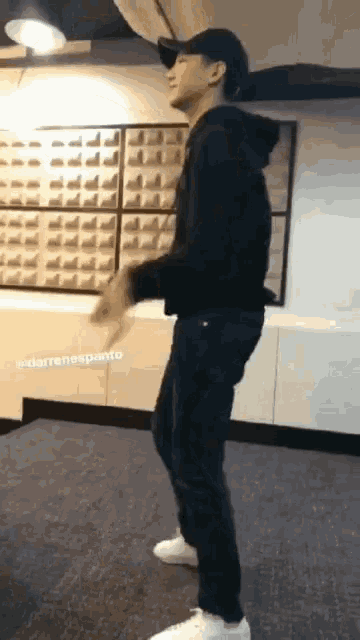 a man wearing a black hoodie and white sneakers is dancing in a room