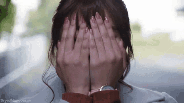 a woman covering her face with her hands with the website dryedmangoez.com visible in the background