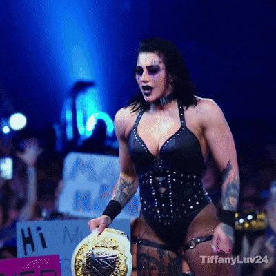 a woman in a black bodysuit is holding a gold wrestling championship belt and a sign that says hi