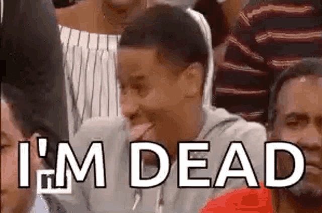 a man is sitting in a crowd with his tongue out and the words `` i 'm dead '' written on his face .