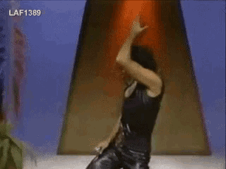 a man in a black leather outfit is dancing in a room with a plant .