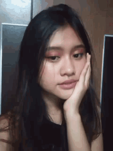 a girl with long black hair is holding her hand to her face .