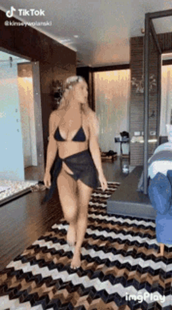a woman in a bikini and skirt is walking on a rug in a room .