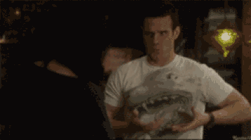 a man in a white t-shirt with a shark on it is talking to another man .