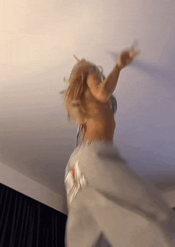 a woman in a bra and sweatpants is dancing in a room with her hands in the air .