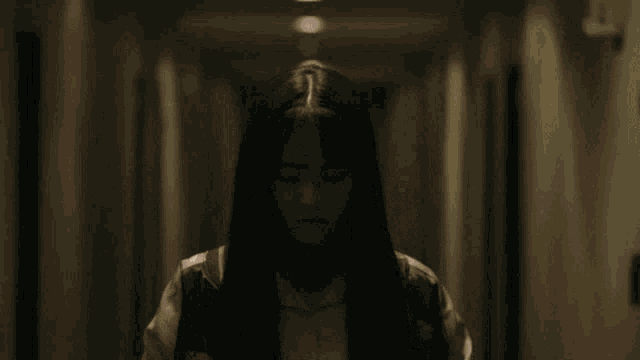 a girl with long hair and glasses stands in a hallway