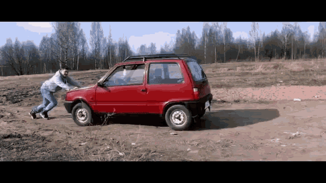 a man is pushing a small red car in a dirt field