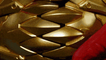 a close up of a gold colored object with a red object in the background