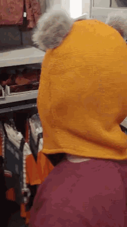 a person wearing a yellow hooded hat looks at clothes