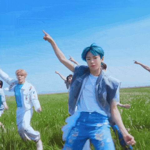 a boy with blue hair is dancing in a field with other people