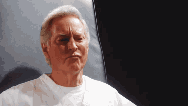 a man in a white shirt is looking at the camera with a serious look on his face