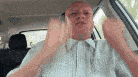 a bald man is sitting in the back seat of a car making a face .