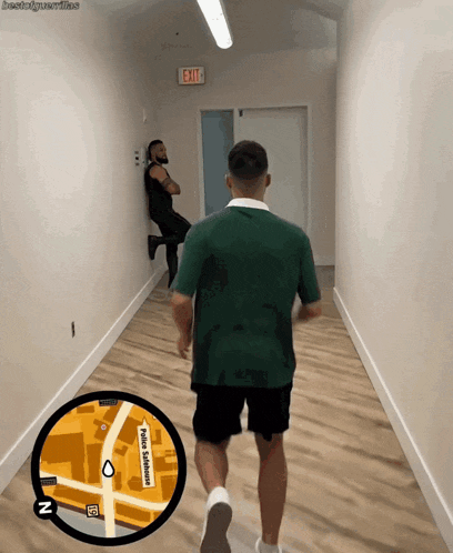 a man in a green shirt is walking down a hallway with an exit sign in the background