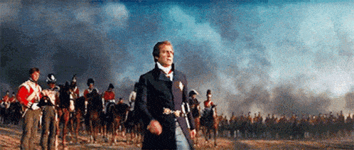 a man is walking in front of a large army of men on horseback .