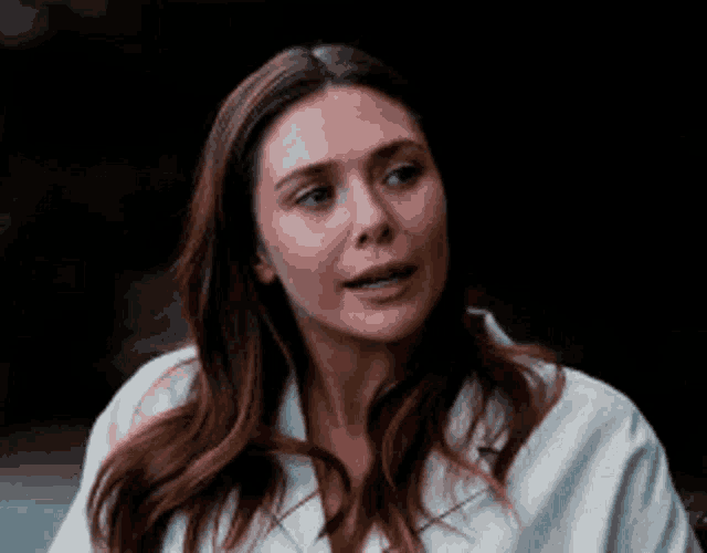 a woman with long brown hair and a white shirt is looking at the camera .