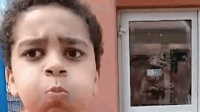 a young boy is making a funny face while standing in front of a window .