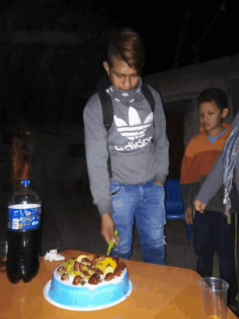 a man wearing a grey adidas sweatshirt is cutting a cake