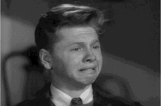 a black and white photo of a young man in a suit and tie making a funny face .