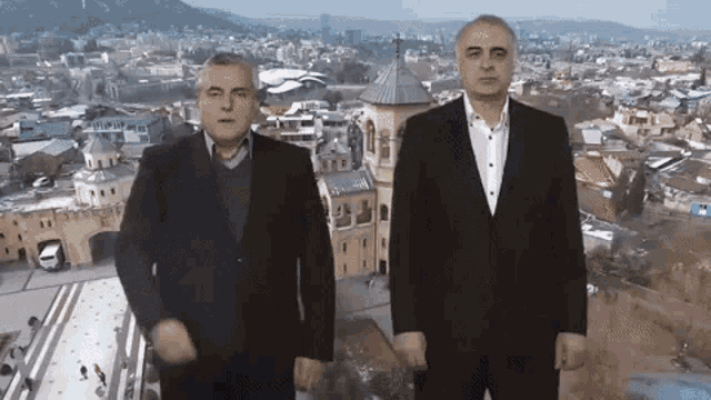 two men standing in front of a city with a tower in the background