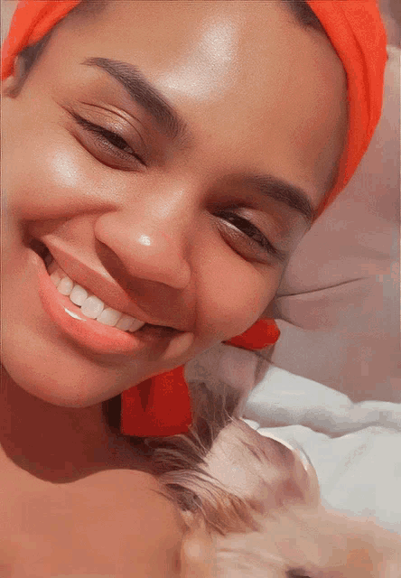 a woman wearing a red headband smiles while laying next to a small dog