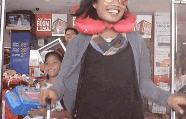 a woman wearing a red neck pillow stands in front of a store with a boom sale sign