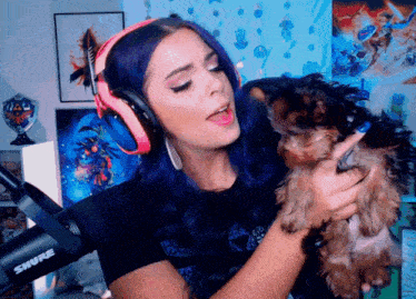a woman wearing pink headphones holds a small dog in front of a shure microphone