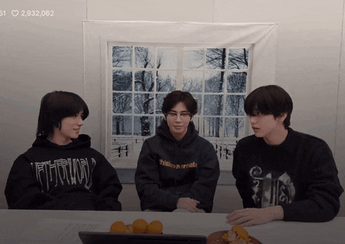 three young men are sitting at a table and one of them has a hoodie that says " ftth " on it