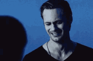 a man wearing a black shirt is smiling in front of a blue background