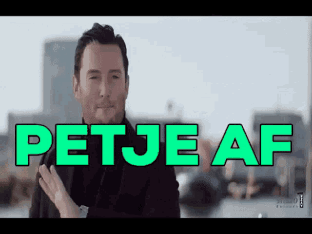 a man in a black coat stands in front of a green sign that reads petje af