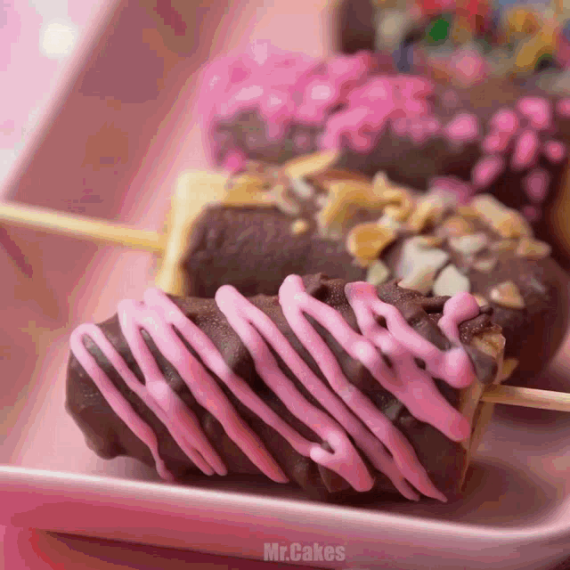 a close up of a chocolate donut with pink icing and the words mr.cakes below it