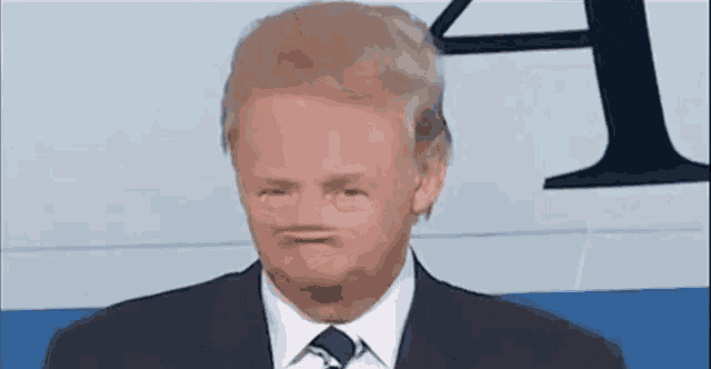 a man in a suit and tie is making a funny face in front of a sign .