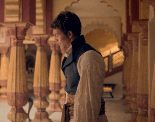 a man in a white shirt and a black vest stands in a hallway