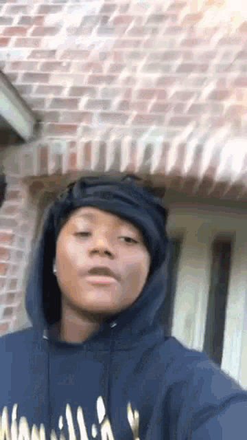 a young woman wearing a hoodie is taking a selfie in front of a brick wall .