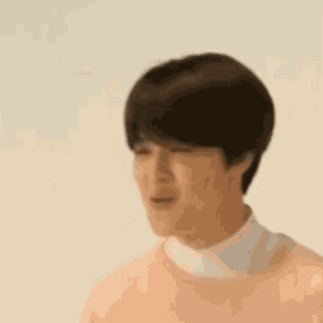 a young man wearing a pink sweater and a white turtleneck is making a funny face .