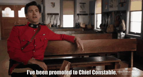 a man in a red uniform is sitting on a bench and says i 've been promoted to chief constable