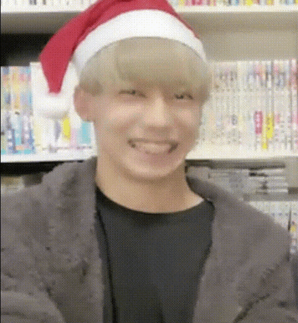 a young man wearing a santa hat is smiling in front of a book shelf .