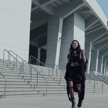 a woman in a black dress is walking down stairs in front of a building