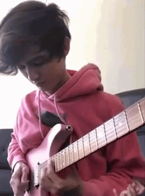 a boy in a pink hoodie is playing a pink guitar .