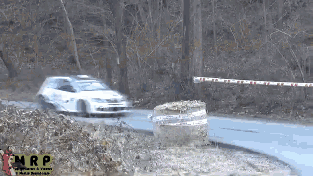 a white car is driving down a road with a mrp logo behind it