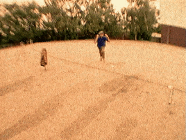 a man in a blue shirt is running on a sandy surface