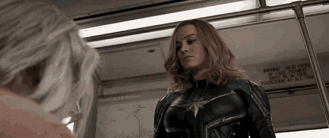 a woman in a superhero costume is standing next to another woman on a subway .