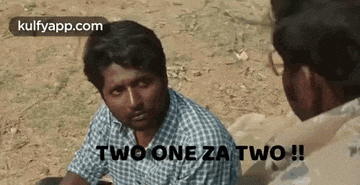 a man in a plaid shirt is talking to another man while sitting on the ground .