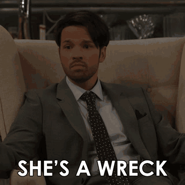 a man in a suit and tie is sitting on a couch with the words she 's a wreck below him