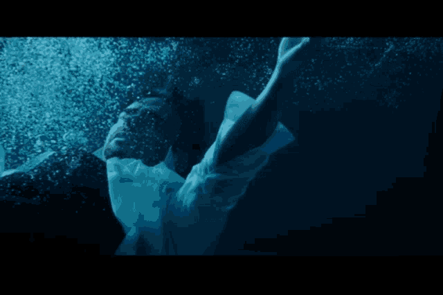a person in a white shirt is swimming under water